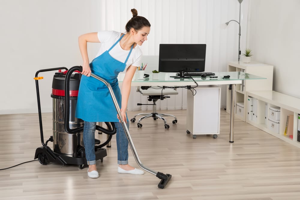 Female Janitor Cleaning Floor with Vacuum Cleaner In Office
