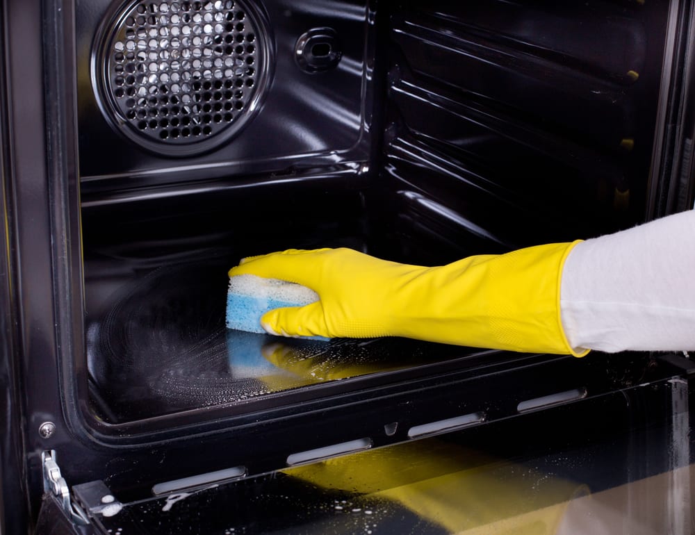 Close up of female hand with yellow protective gloves cleaning oven